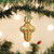 Image shows a mini cross ornament that is blown from glass and hand-painted with shimmering gold and silver accents hanging on a tree branch.
