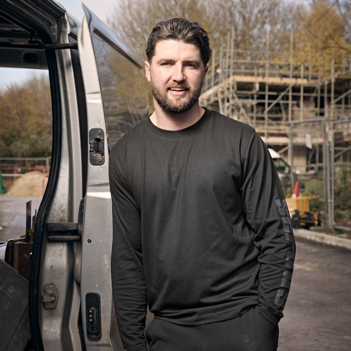 Tradesman leaning against work van wearing black Scruffs Winslow Long Sleeve T-Shirt