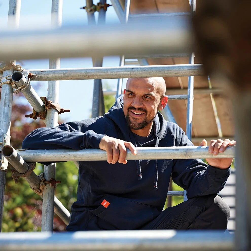 Scruffs Worker Hoodie navy worn by tradesman on scaffolding showing durable workwear design, drawstring hood and kangaroo pocket