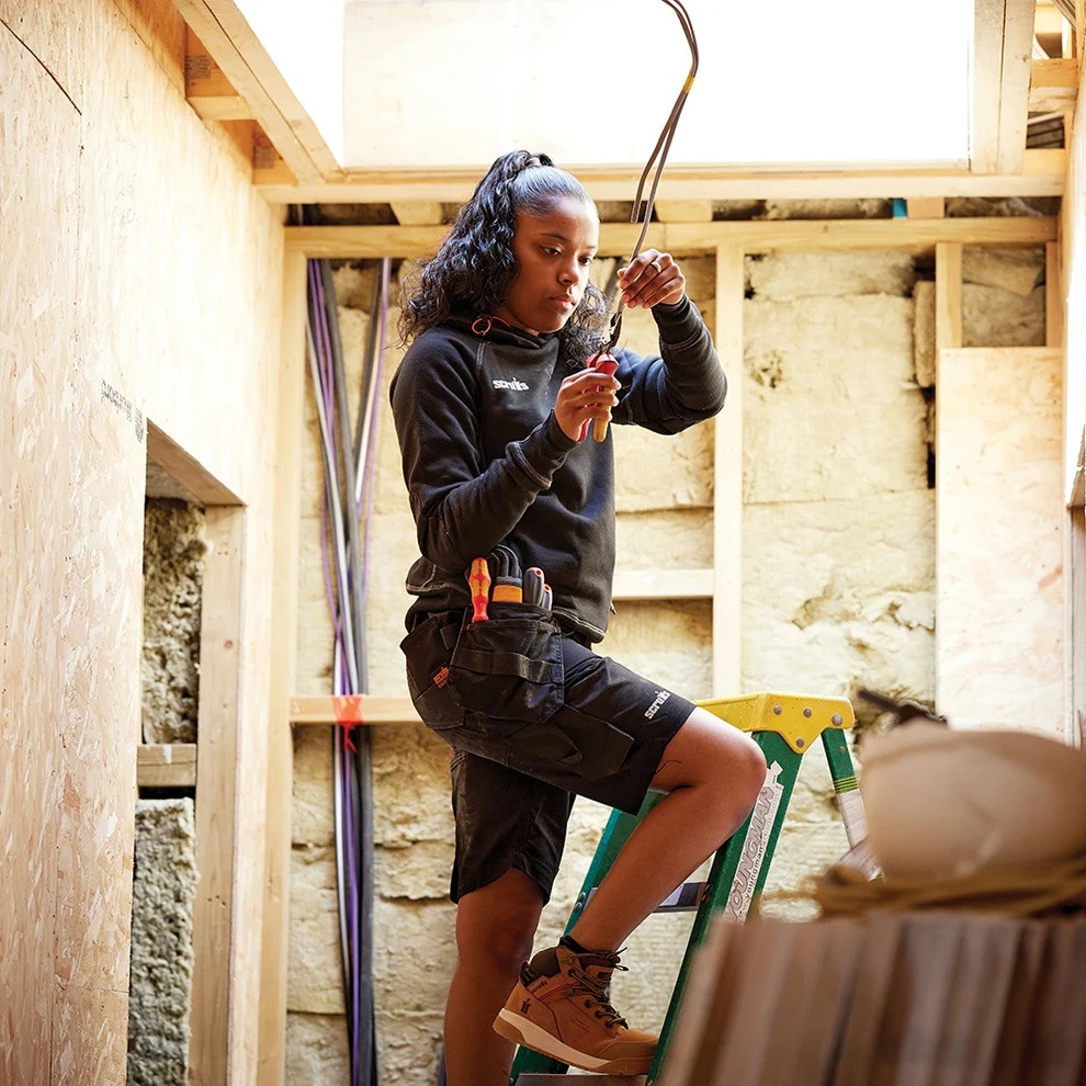 Scruffs Women's Trade Flex Holster Shorts worn on a construction site with tool pockets and flexible workwear fit