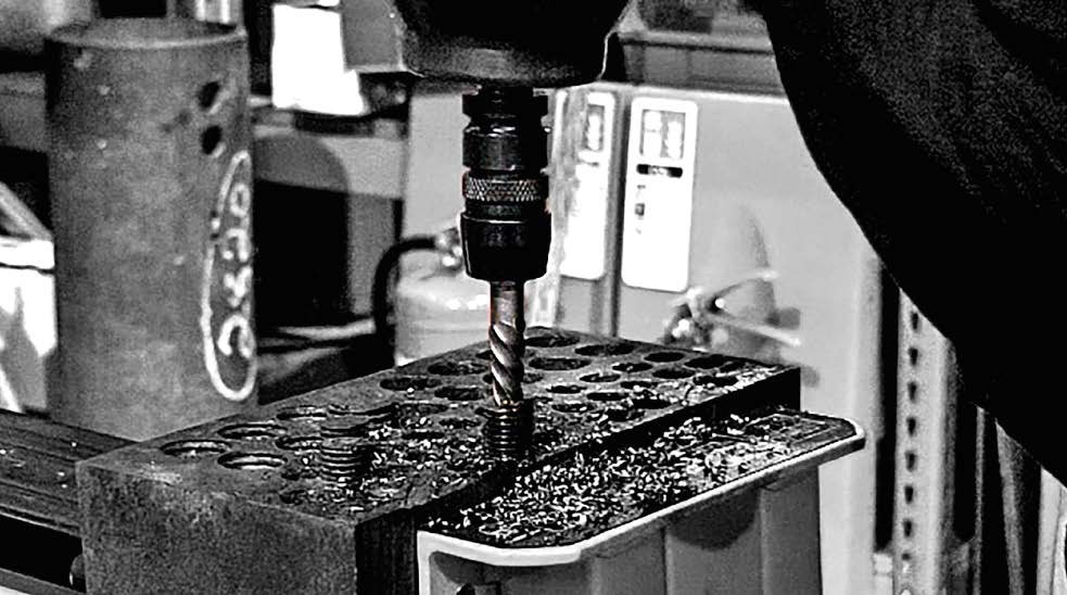 Black and white close-up of extractor tool drilling into metal on a drill press