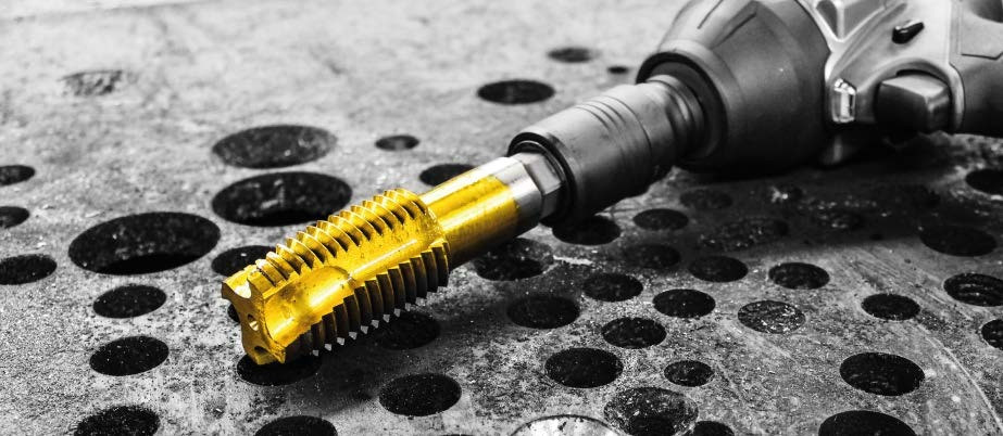 Gold spiral point tap fitted to an impact wrench beside drilled steel plate