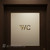 A modern, chrome gold 'WC' sign sticker with a subtle black shadow effect