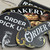 Close-up of assorted custom hanging business signs showing black sign surfaces, decorative lettering, and gold ornamental detailing.