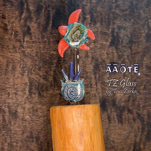 Flameworked glass art sculpture by AAOTE's founder, Tari Zarka. Totally one-of-a-kind, investment-quality glass art on a wooden base. 

The Sea Turtle is a Fidget Widget design with sherbert fins and a spikey leaf accent. It's a 3-piece set including the wood base. The overall size is approximately 9"H x 3.5"W x 3"D.

There is only one available. The piece you see is the piece you get. It will arrive dissassebled. The glass pieces slide out of the base, and get wrapped separate from the base for safe shipment. Assembly is as easy as sliding the glass rods into the wooden base. 

The wooden base is actually crafted from fallen timber from AAOTE's property. 

This sculpture will ship USPS Priority with insurance and is not eligible for free shipping offers.