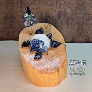 Flameworked glass art sculpture by AAOTE's founder, Tari Zarka. Totally one-of-a-kind, investment-quality glass art on a wooden base.
Sea Turtle with wave design with a leaf accent. It's a 3-piece set including the wood base. The overall size is approximately 5.75"H x 4.5"W x 5"D.
There is only one available. The piece you see is the piece you get. It will arrive dissassebled. The glass pieces slide out on the base, and gets wrapped separate from the base for safe shipment. Assembly is as easy as placing the glass onto the wooden base.
The wooden base is actually crafted from fallen timber from AAOTE's property.
This sculpture will ship USPS Priority with insurance and is not eligible for free shipping offers. Flameworked glass art sculpture by AAOTE's founder, Tari Zarka. Totally one-of-a-kind, investment-quality glass art on a wooden base.
Sea Turtle with wave design with a leaf accent. It's a 3-piece set including the wood base. The overall size is approximately 5.75"H x 4.5"W x 5"D.
There is only one available. The piece you see is the piece you get. It will arrive dissassebled. The glass pieces slide out on the base, and gets wrapped separate from the base for safe shipment. Assembly is as easy as placing the glass onto the wooden base.
The wooden base is actually crafted from fallen timber from AAOTE's property.
This sculpture will ship USPS Priority with insurance and is not eligible for free shipping offers.