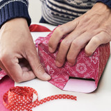 A pair of hands wrapping a gift in vibrant pink personalised gift wrapping paper, with red polka dot ribbon nearby.