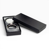 A silver keychain displayed in a black gift box, featuring a sleek design and a glossy finish.