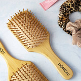 A bamboo hairbrush with a wide paddle design and wooden bristles, accompanied by hair accessories and a tube.
