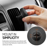 A round black car phone holder with a logo, being attached to an air vent by a hand.