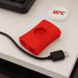 A red Snappi 1 Piece Cable Manager on a desk, with a black USB cable beside it.