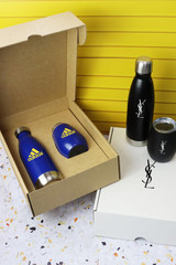 A drink bottle set featuring a blue stainless steel bottle, a black stainless steel bottle, and a glass tumbler, all in packaging.