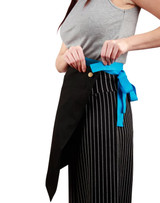 A half waist apron in black with a blue tie, worn by a person adjusting the waistband. Features a logo.
