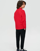 A child wearing black track pants and a red long-sleeve shirt, standing with their back to the camera.