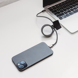 A charging cable in black and grey connected to a smartphone and a laptop on a desk.