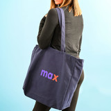 A navy blue tote bag with a logo on the side, being carried by a person from behind.