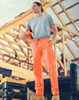 Lightweight nylon waterproof rain pants in bright orange, modelled by a person on a construction site.