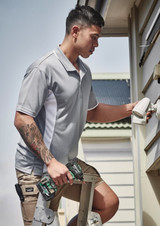 A man in a grey short sleeve polo shirt adjusts a fixture while standing on a ladder, holding tools.