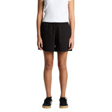 Black track shorts with a relaxed fit, featuring an elastic waistband and side pockets. Model is standing.