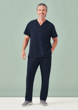 A man wearing navy unisex scrub pants and a matching short-sleeve top, standing against a light green background.