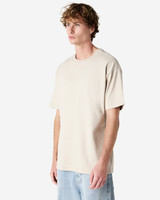 A beige super heavyweight T-shirt displayed on a model, featuring a relaxed fit and short sleeves.
