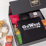 A gift pack featuring assorted gourmet treats, a black branded tote bag, and colourful packaging.