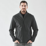 A man wearing a black softshell jacket with a zip front and side pockets, standing against a plain background.