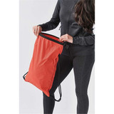 A red drawstring bag is being held by a person in a black outfit. The bag features a contrasting black edge and straps.