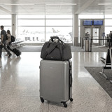 A grey High Sierra travel duffel rests on top of a silver suitcase in an airport terminal. It features a logo.