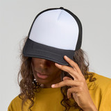 A black and white trucker cap featuring a flat brim and mesh back, worn by a person with long, curly hair.