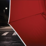 A red compact umbrella with a sleek design, partially opened against a night city backdrop and street lighting.