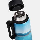 A drink bottle with a blue and scenic design, featuring a black handle and a stainless steel opening.