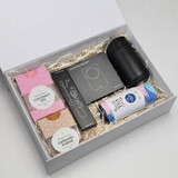 A gift box containing a black drink bottle, snacks, and a card set, all set on shredded paper packaging.