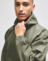 A man wearing a green Champion packable anorak jacket with a hood, featuring a logo on the sleeve.