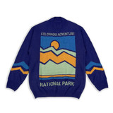 A blue knitted jumper featuring a mountain design with orange and yellow accents, and a branding logo.