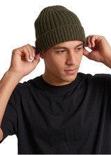 A green beanie is being worn by a person adjusting it while dressed in a black T-shirt.
