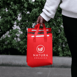 A red insulated reusable bag with two handles, featuring a logo on the front, held by a person.