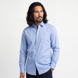 A man in a light blue long-sleeve shirt stands against a neutral background. The shirt features a collar and buttons.