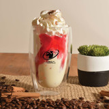 A double wall glass cup featuring a logo, filled with a dessert topped with whipped cream and strawberry sauce.