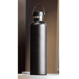 A drink bottle made of stainless steel, featuring a matte black finish and a carrying handle. It has a logo on the side.