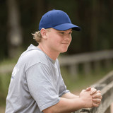 A blue Falcon Flex Cap worn by a young person, who is sitting outdoors by a wooden railing.