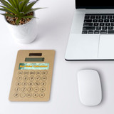 An eco-friendly solar calculator in a natural beige colour, placed alongside a laptop and plant on a desk.