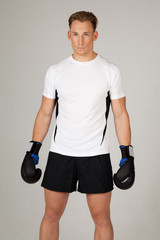 A man poses in a white and black short-sleeved T-shirt, wearing boxing gloves and black shorts.