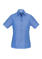 A blue chambray short sleeve button-up shirt with a front pocket and button detailing. It has a logo on the label.