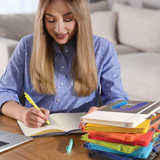 A stack of Venture Bondi A5 Notebooks in various colors, with a person writing in one of the notebooks.
