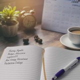 An open notebook with lined pages, a purple pen, a coffee cup, and a plant on a wooden desk.