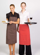 Two women wearing striped aprons, one brown and one red, holding a cup and a tray with a glass of wine.