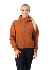 A woman wearing an orange-brown half-zip jumper with a hood, posing against a white background.