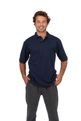 A navy blue men's cotton pique knit polo shirt displayed on a smiling man wearing grey trousers. The shirt features a logo.