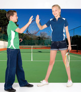 A boy in a green polo shirt and a girl in a blue polo shirt, both holding tennis rackets on a court.